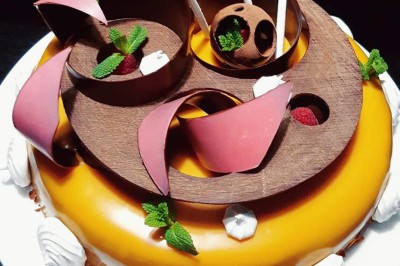 Gâteau décoré de glaçage caramel, éléments en chocolat, framboises et feuilles de menthe sur une assiette blanche.