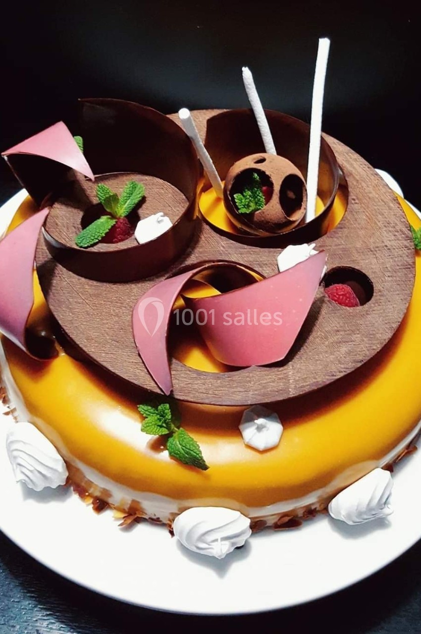 Gâteau décoré de glaçage caramel, éléments en chocolat, framboises et feuilles de menthe sur une assiette blanche.