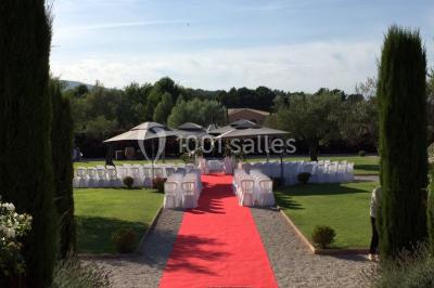 Allée rouge menant à une cérémonie en plein air, entourée de chaises blanches et de jardins verdoyants.