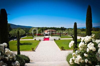 Allée rouge menant à une cérémonie en plein air, entourée de chaises blanches et de jardins verdoyants.
