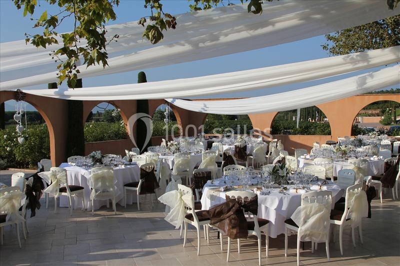 Tables dressées pour un événement en extérieur sous des voiles blanches, avec vue sur un jardin arboré.
