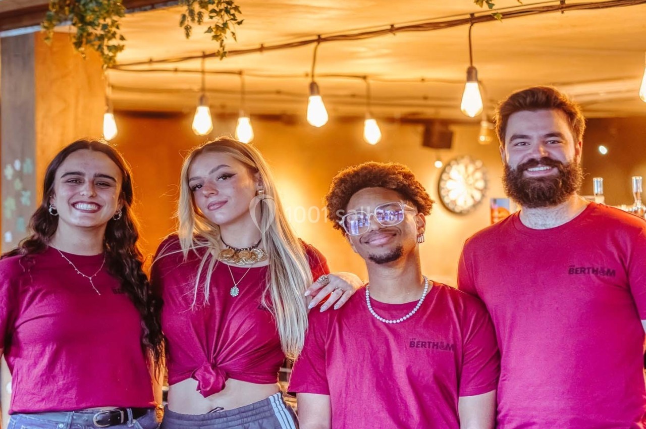 Quatre personnes souriantes portant des t-shirts rouges posent devant un décor chaleureux avec des lumières suspendues.