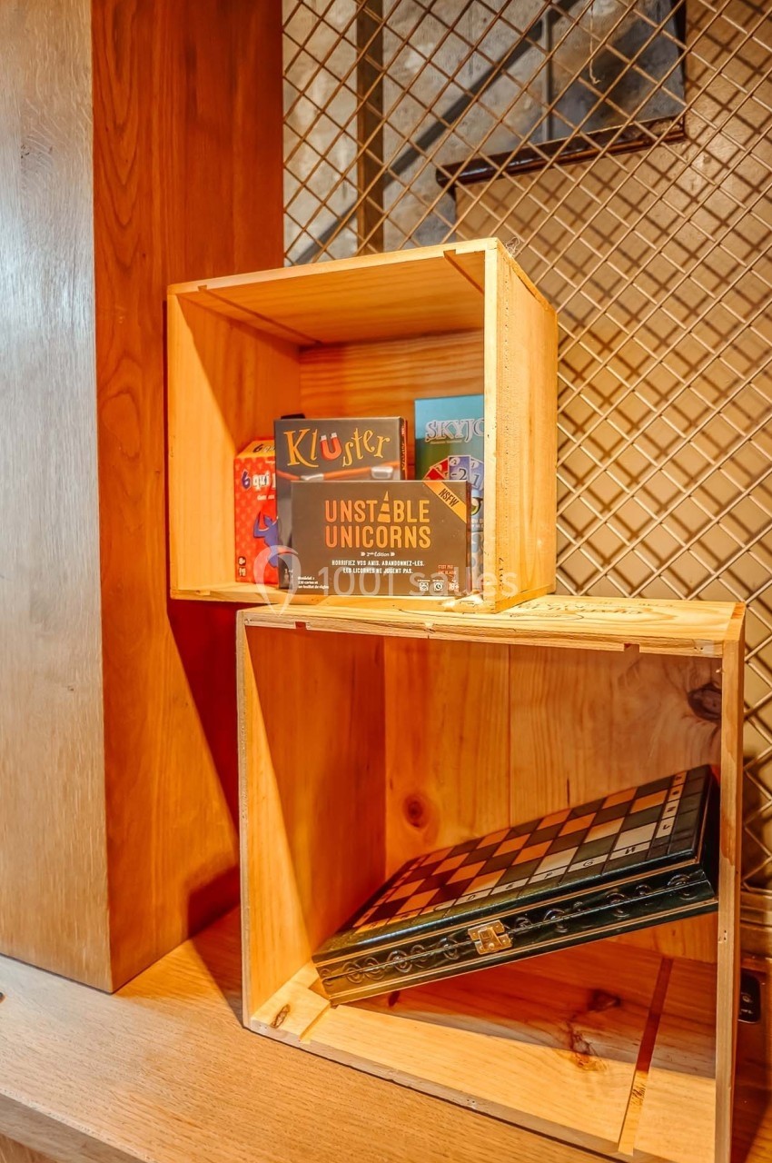 Deux caisses en bois empilées contenant des jeux de société, posées devant un mur à motif quadrillé.