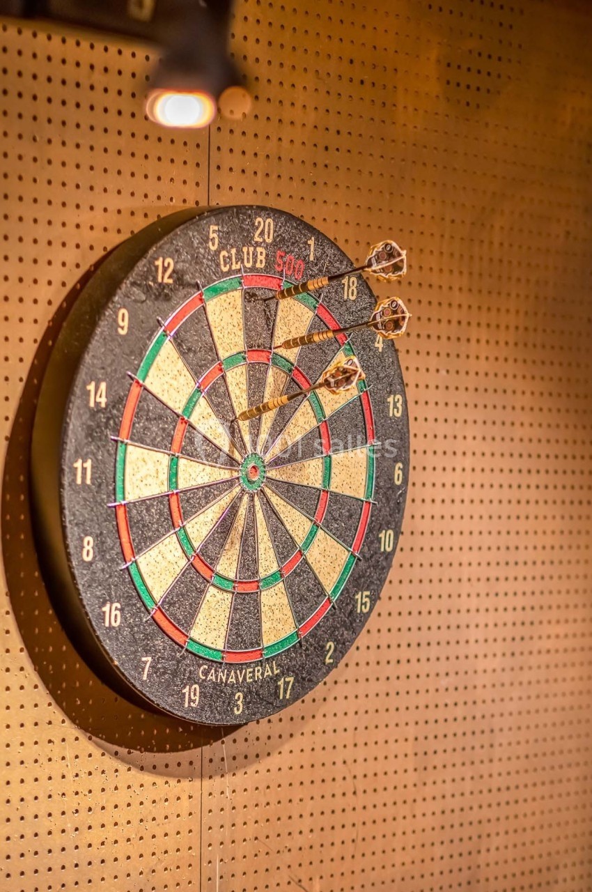 Cible de jeu de fléchettes accrochée à un mur perforé, avec deux fléchettes plantées dans la zone centrale.
