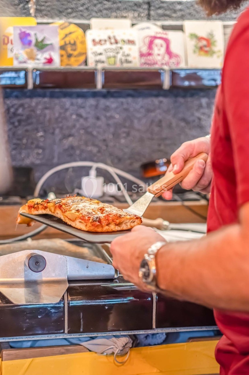 Un cuisinier retire une part de pizza du four à l'aide d'une pelle dans une cuisine.