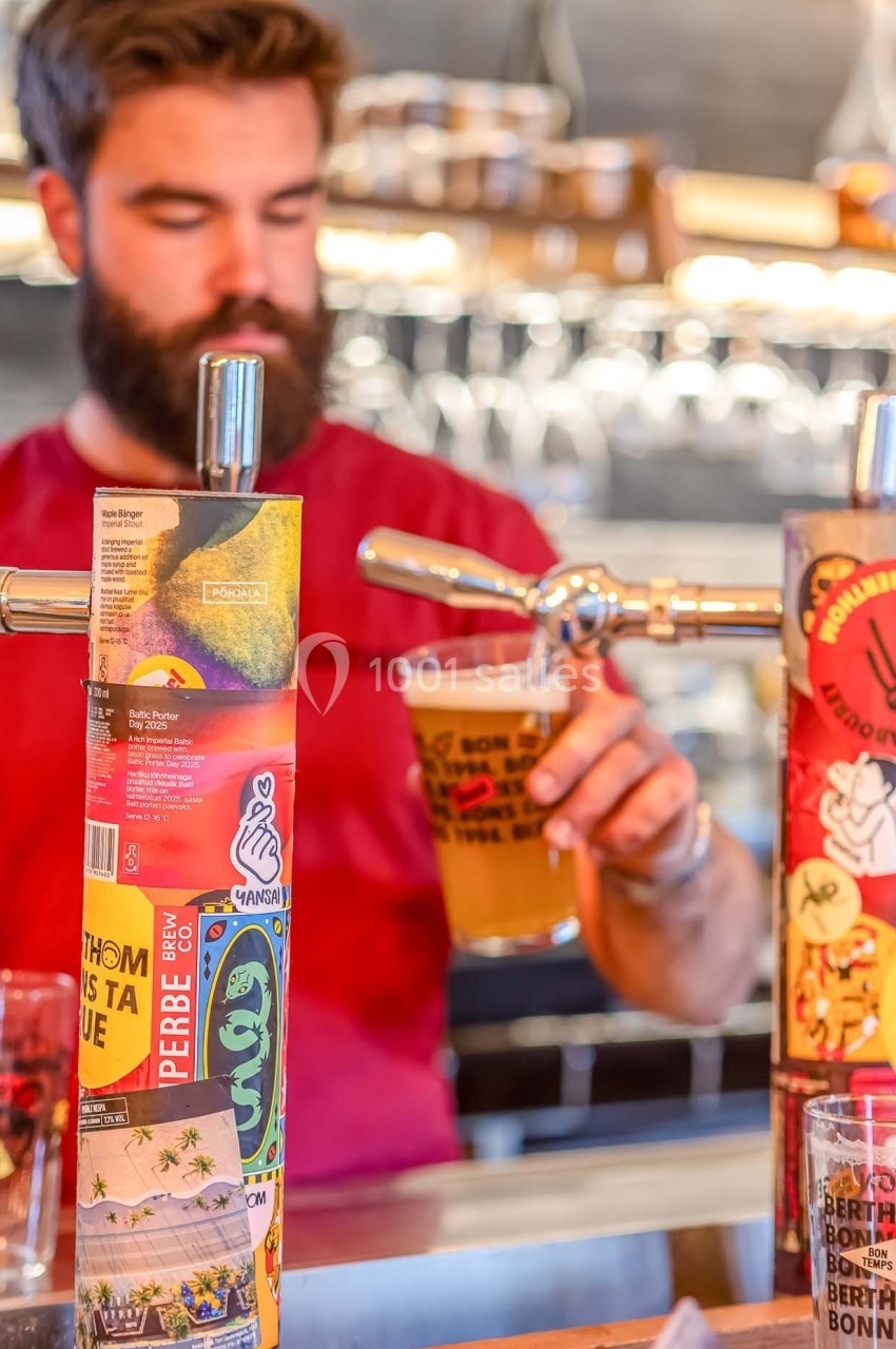 Un barman sert une bière pression dans un verre, avec des tireuses décorées en arrière-plan.