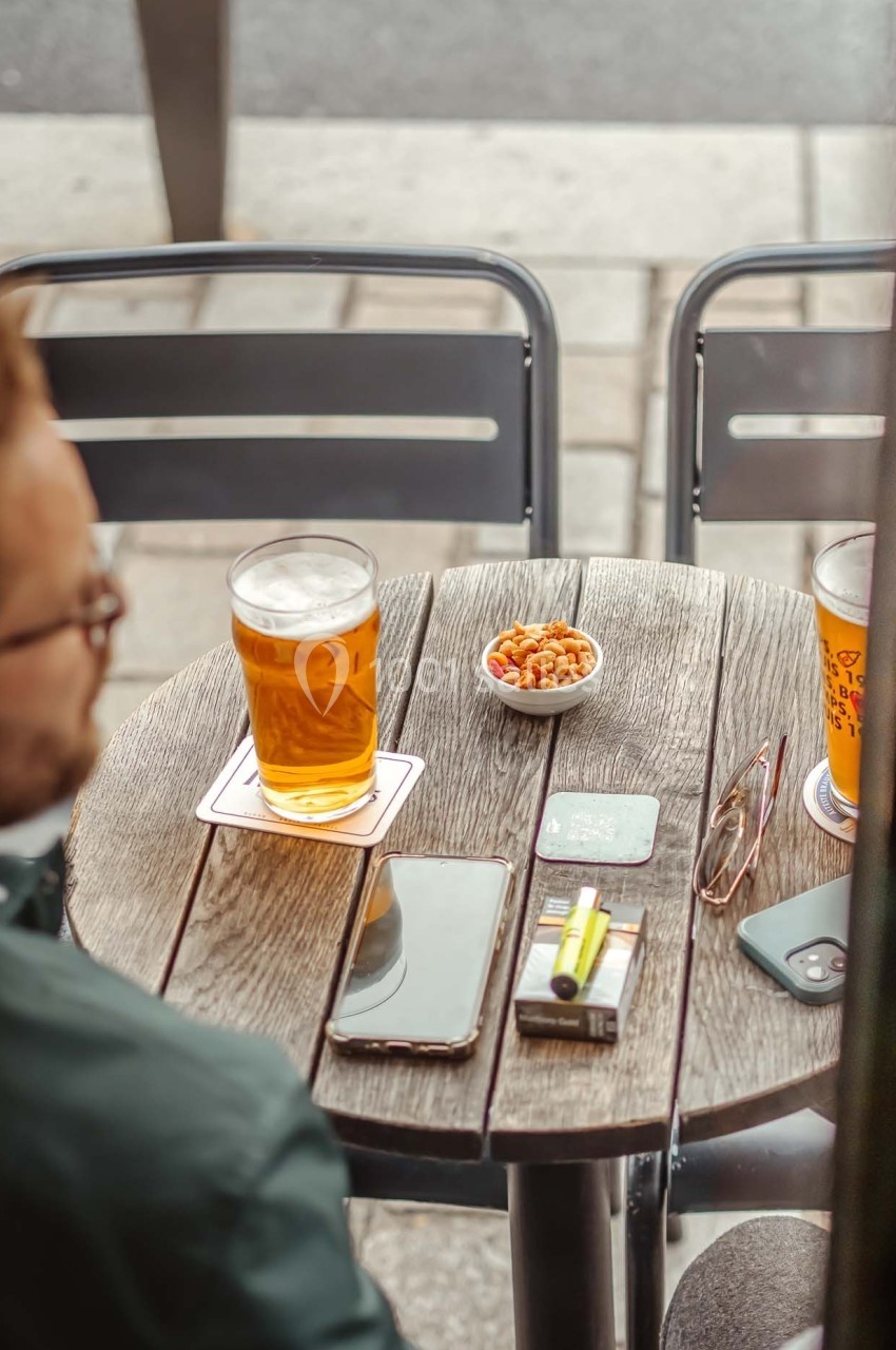 Deux verres de bière, une coupelle de cacahuètes et divers objets personnels sur une table en bois en extérieur.