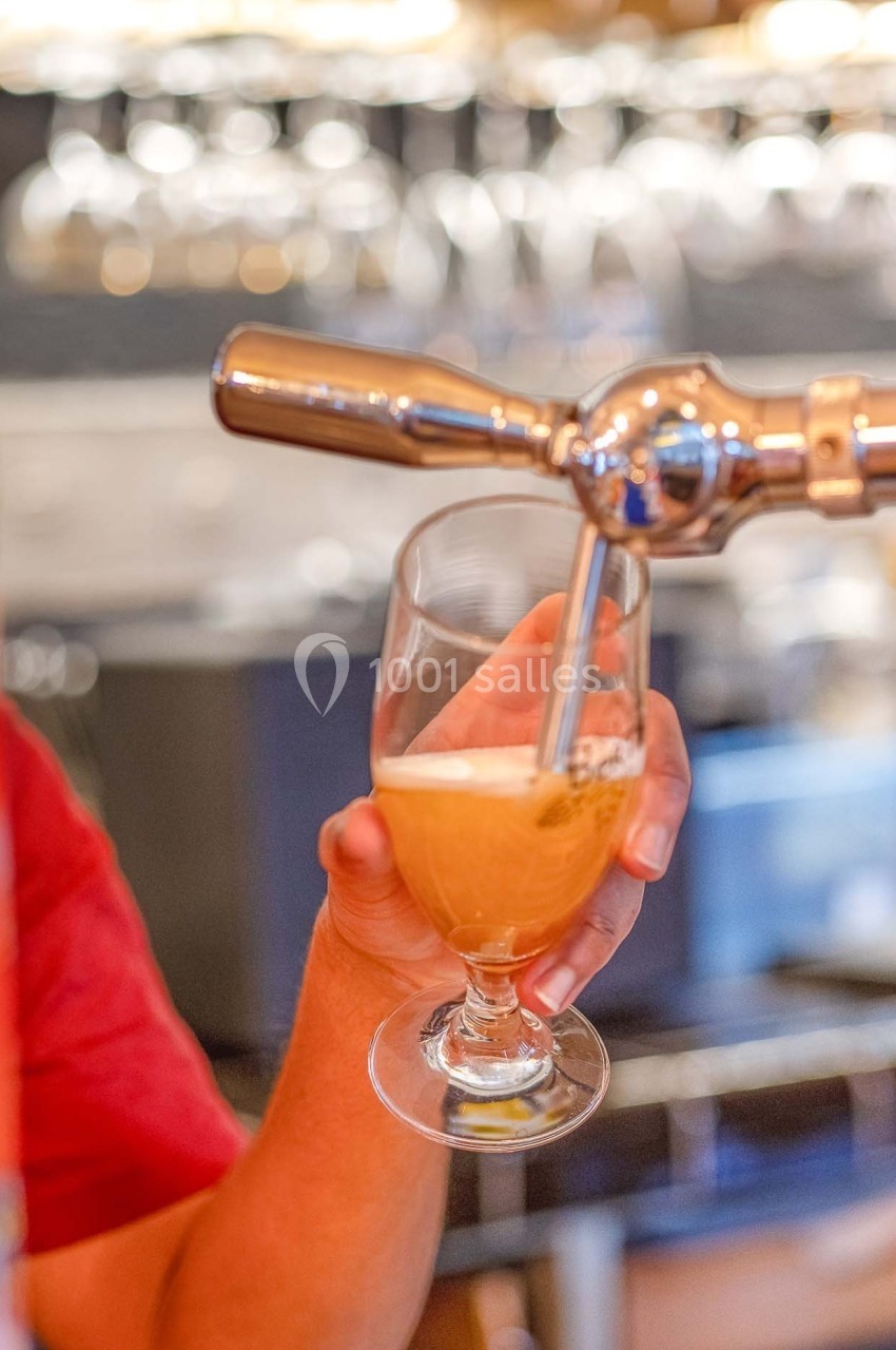 Une main verse de la bière blonde depuis une tireuse dans un verre, avec un arrière-plan flou de bar.