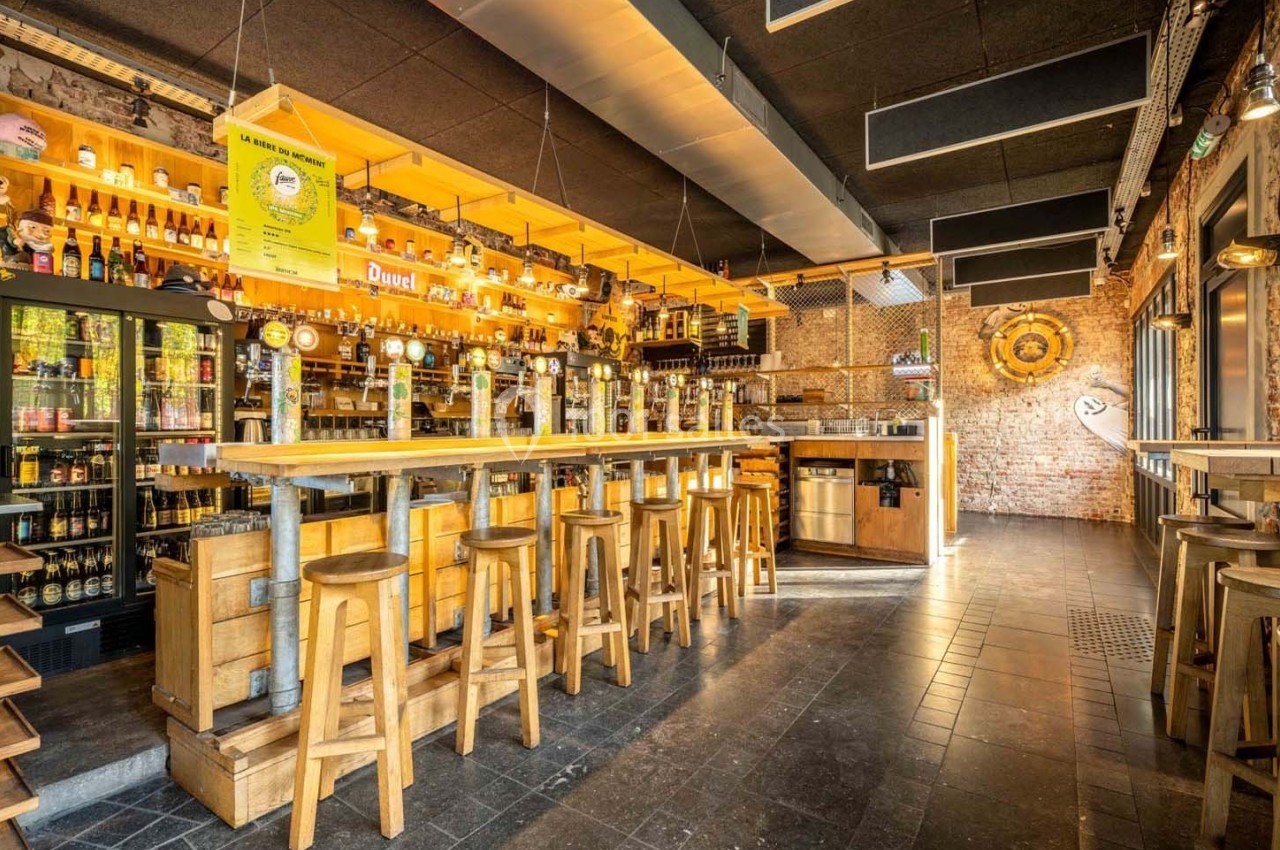 Intérieur d'un bar lumineux avec comptoir en bois, tabourets hauts, étagères remplies de bouteilles et murs en briques.