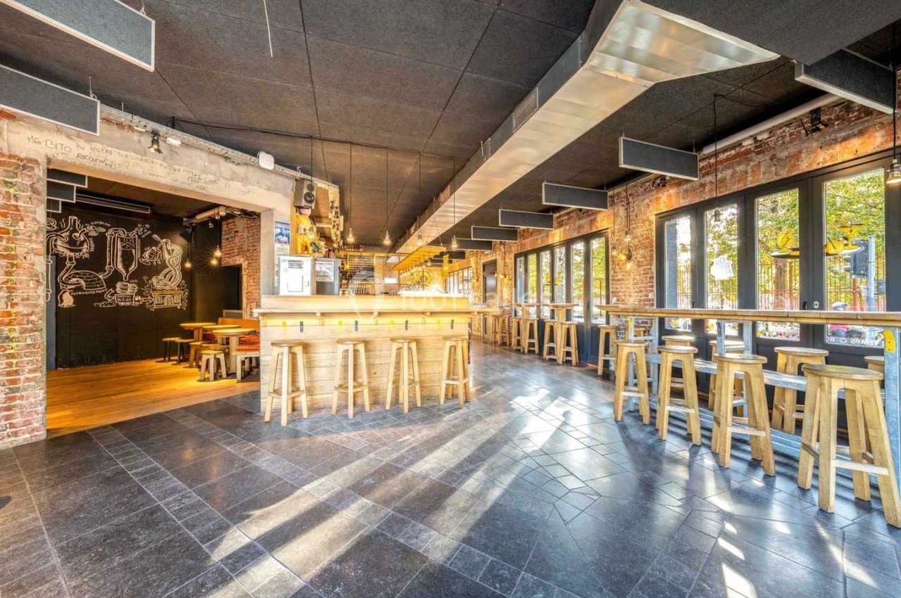 Intérieur lumineux d'un bar avec comptoir en bois, tabourets hauts, murs en briques et grandes fenêtres donnant sur l…