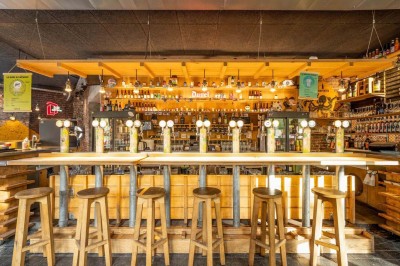 Un couteau et un saucisson sec posé sur une planche en bois, avec un verre de bière en arrière-plan.