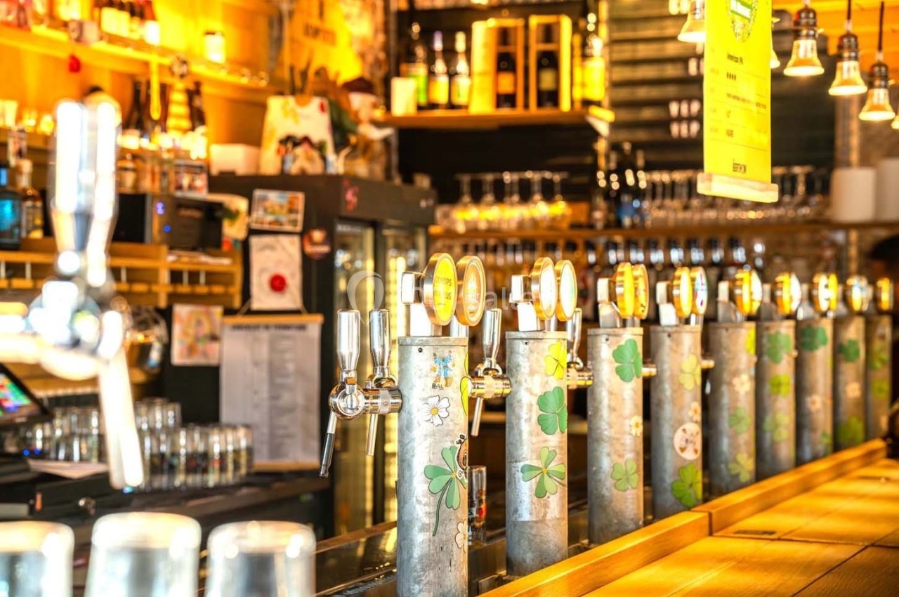 Robinetterie de bière alignée sur un comptoir en bois dans un bar lumineux avec des étagères remplies de bouteilles.