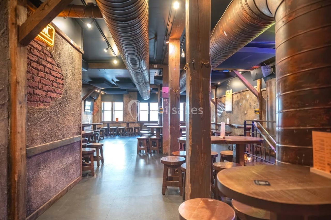 Intérieur d'un bar ou restaurant avec des tables en bois, des murs texturés et un éclairage tamisé.