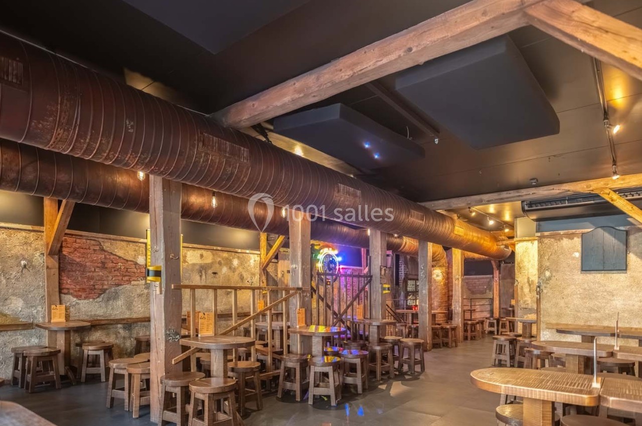 Intérieur d'un bar ou restaurant avec des murs en briques, des poutres en bois et des tables en bois disposées uniformément.