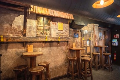 Terrasse d'un café avec des chaises jaunes, des clients attablés et une façade décorée de feuillage automnal.