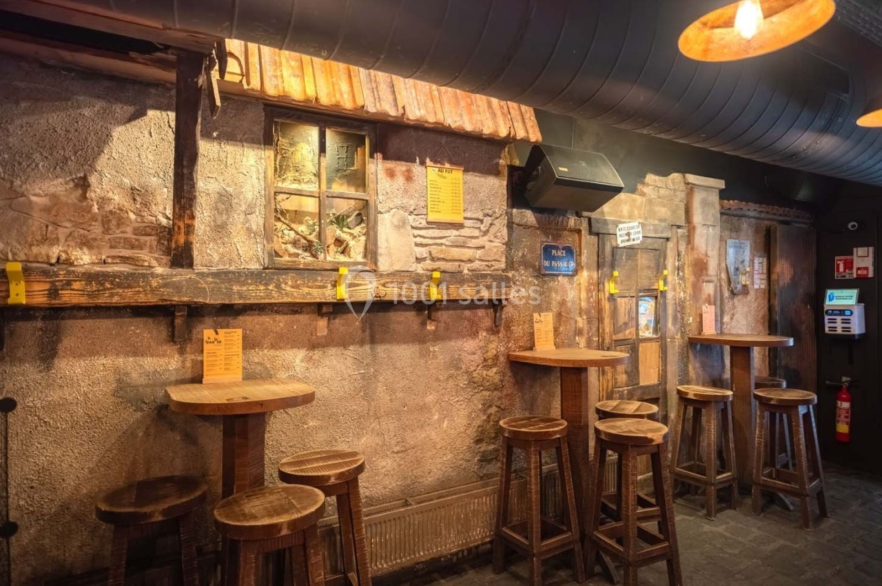 Intérieur d'un bar rustique avec murs en pierre, tables hautes en bois et éclairage chaleureux.