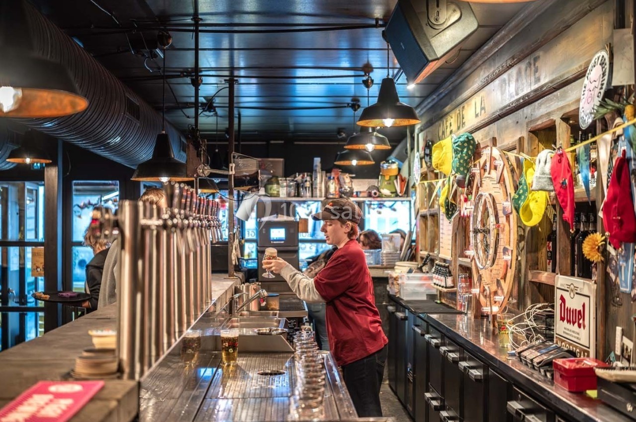Serveuse préparant une boisson derrière un comptoir dans un bar chaleureux avec une décoration éclectique.