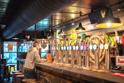 Terrasse d'un café avec des chaises jaunes, des clients attablés et une façade décorée de feuillage automnal.