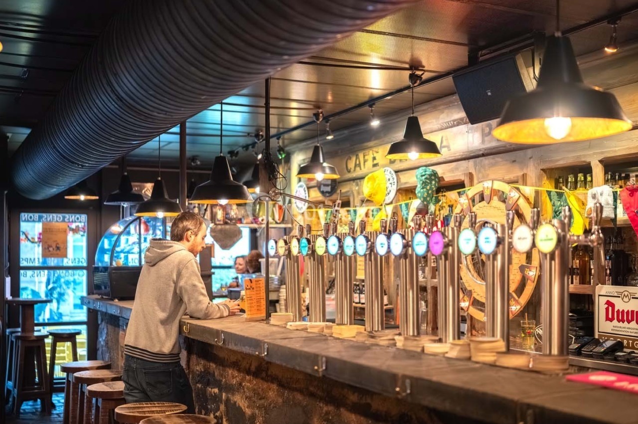 Un homme debout au comptoir d'un bar, entouré de tireuses à bière et d'une ambiance chaleureuse.