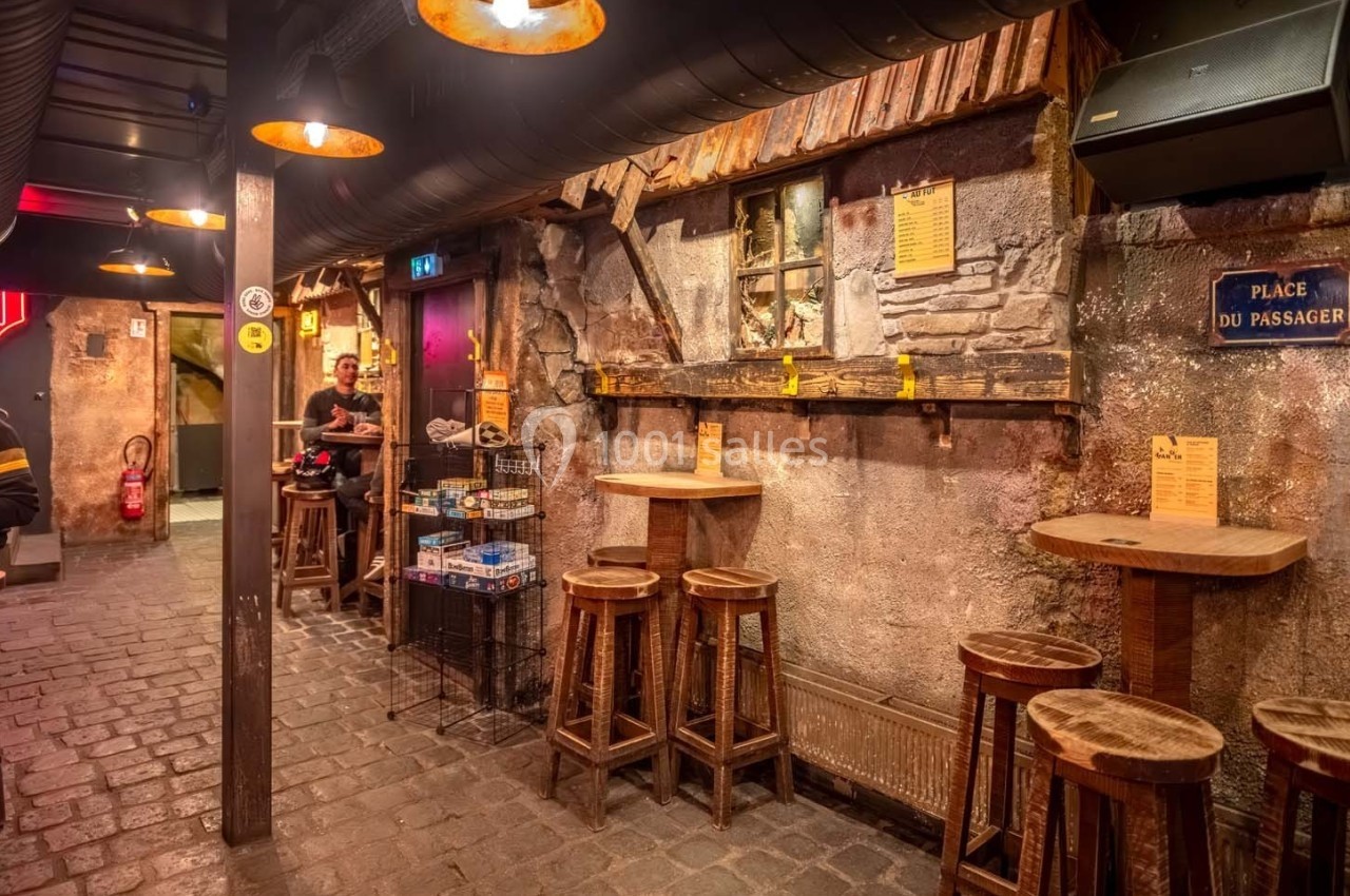 Intérieur d'un bar à l'ambiance rustique avec murs en pierre, tabourets en bois et éclairage chaleureux.
