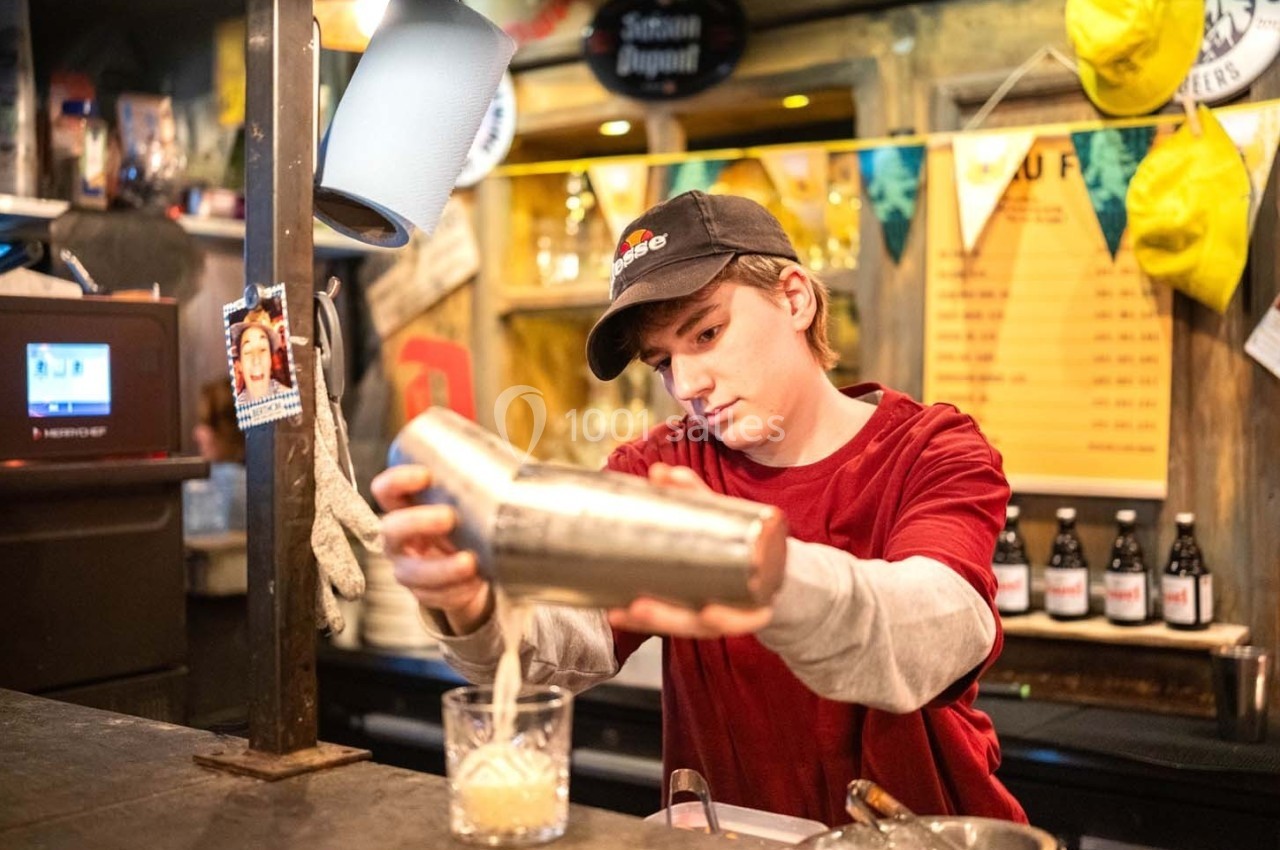 Un barman prépare un cocktail en versant le contenu d'un shaker dans un verre dans un bar animé.