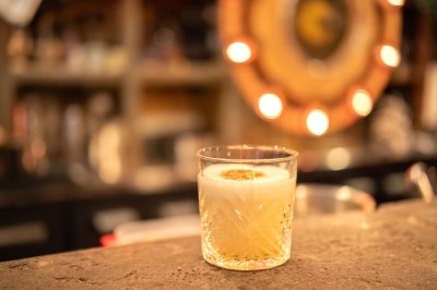 Terrasse d'un café avec des chaises jaunes, des clients attablés et une façade décorée de feuillage automnal.
