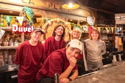 Terrasse d'un café avec des chaises jaunes, des clients attablés et une façade décorée de feuillage automnal.