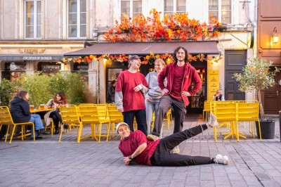 Terrasse d'un café avec des chaises jaunes, des clients attablés et une façade décorée de feuillage automnal.
