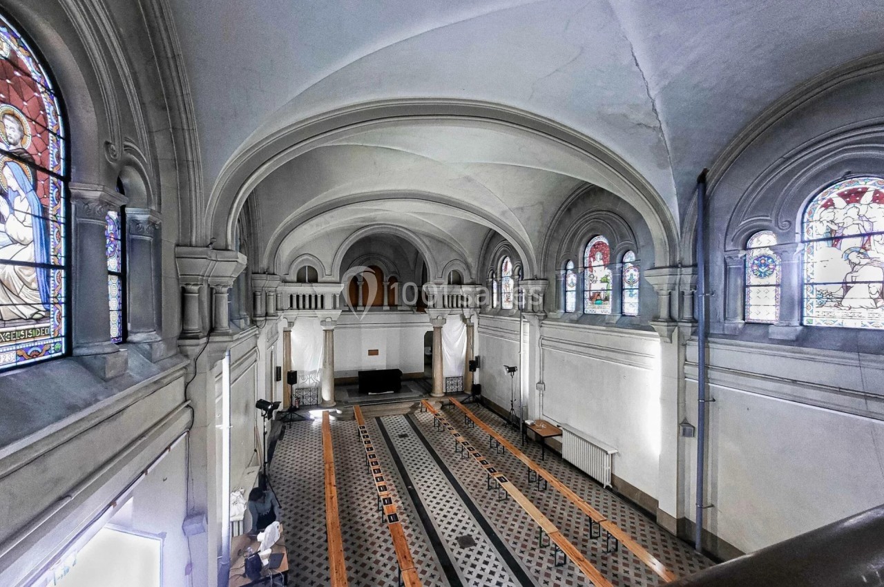 Vue intérieure d'une église avec des bancs en bois, des vitraux colorés et une architecture voûtée.