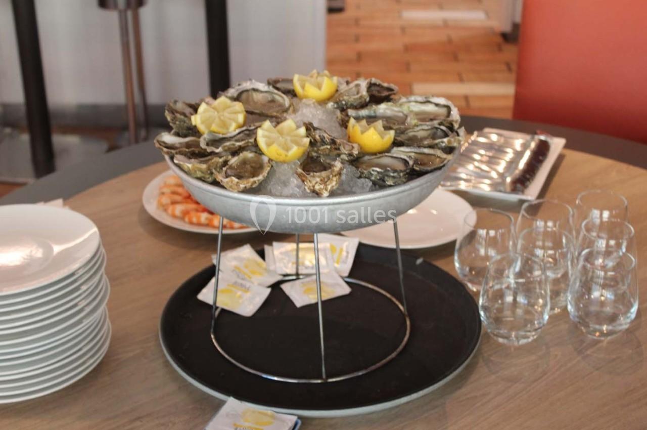 Plateau d'huîtres sur glace avec quartiers de citron, entouré de verres, assiettes et sachets de condiments.