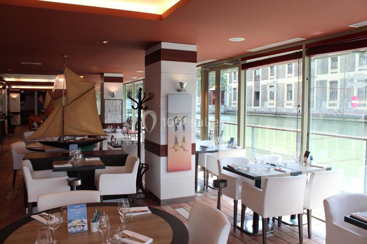 Salle de restaurant lumineuse avec vue sur un canal, tables dressées et décoration nautique.