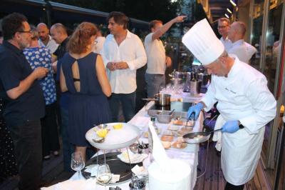 Des personnes dînent en terrasse au bord d'un canal, près d'un restaurant éclairé en soirée.