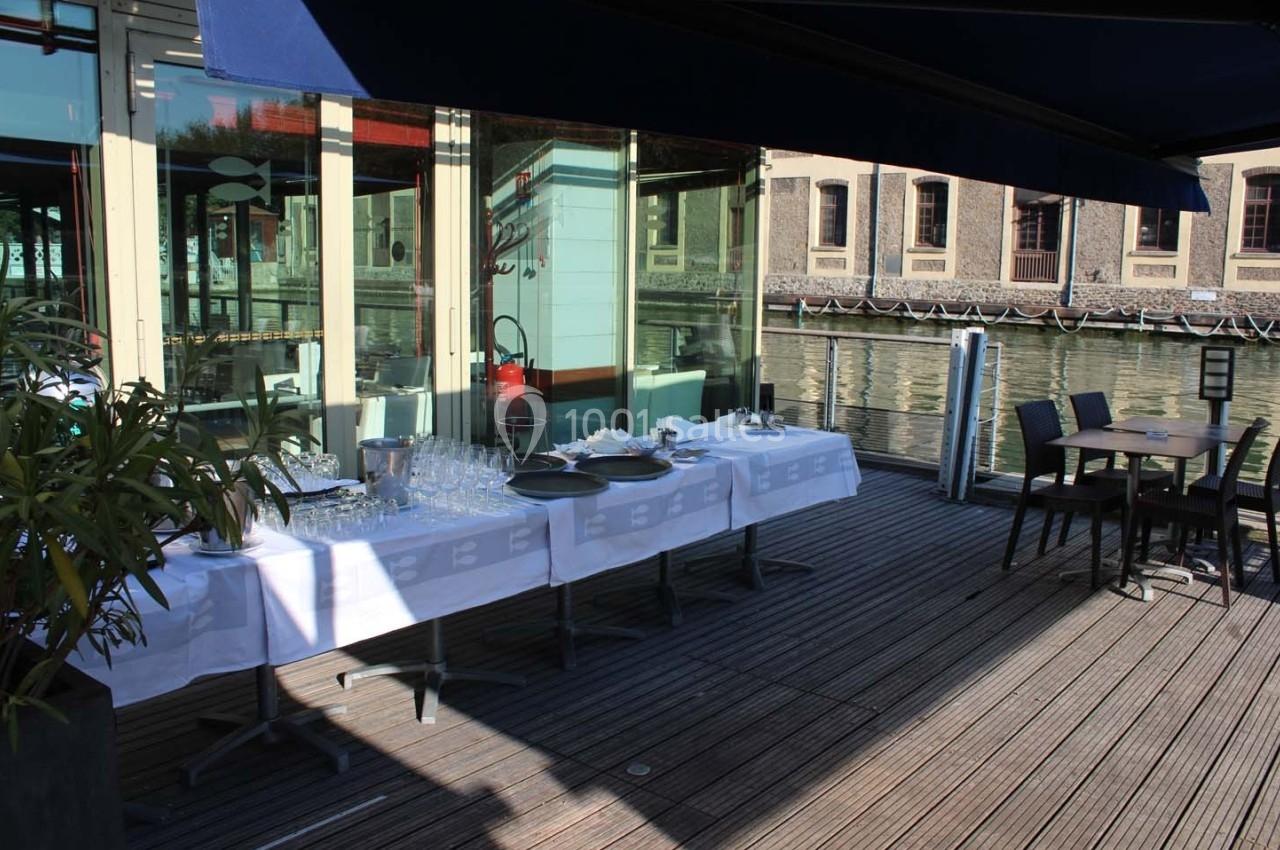 Terrasse en bois avec table dressée pour un buffet, vue sur un canal et bâtiments en arrière-plan.