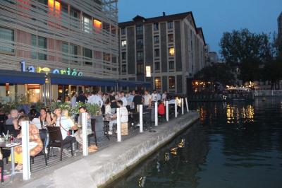 Des personnes dînent en terrasse au bord d'un canal, près d'un restaurant éclairé en soirée.