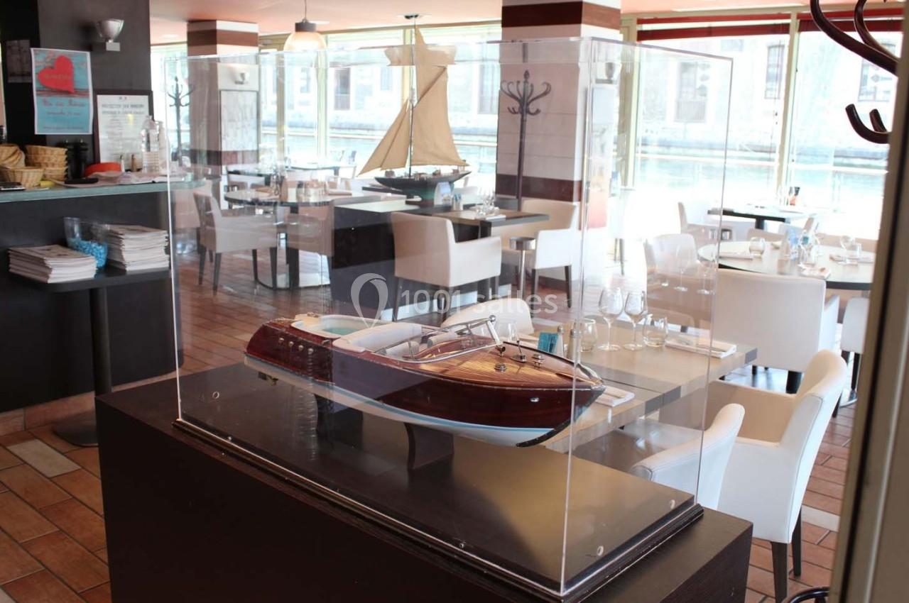 Maquette de bateau en bois exposée sous une vitrine dans un restaurant lumineux avec vue sur l'extérieur.