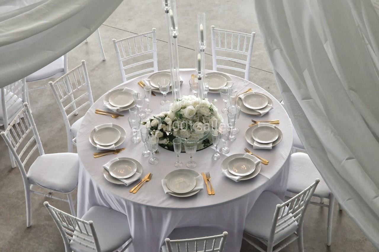 Table ronde élégamment dressée avec nappes blanches, couverts dorés, assiettes, verres et centre de table floral.