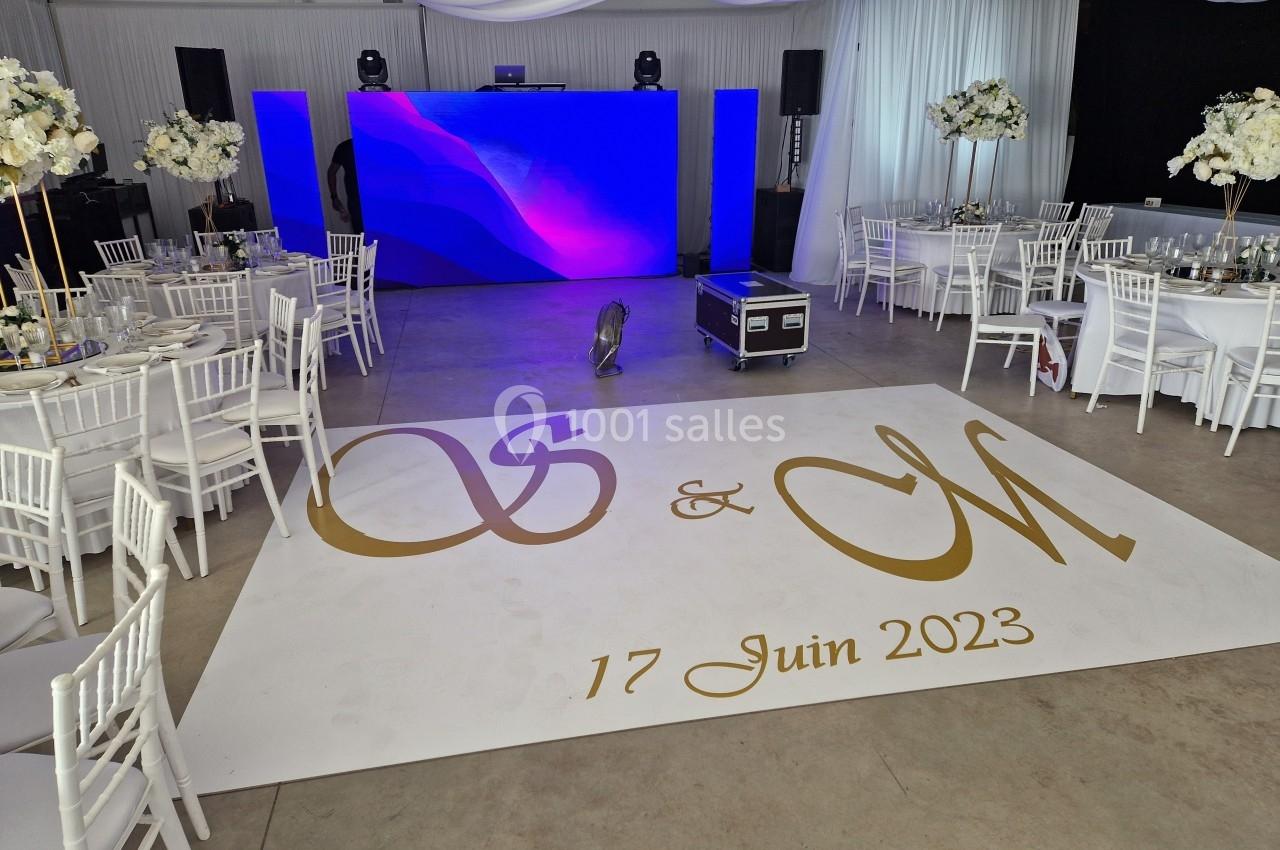 Salle de réception décorée avec tables blanches, piste personnalisée avec initiales dorées et date, écran lumineux en fond.