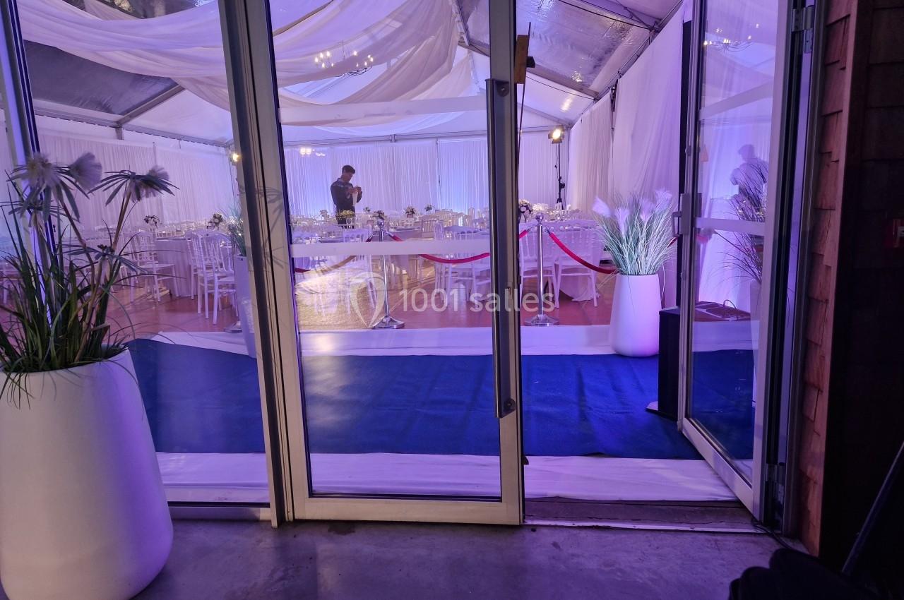 Vue intérieure d'une tente de réception décorée avec des tables dressées et un éclairage violet tamisé.