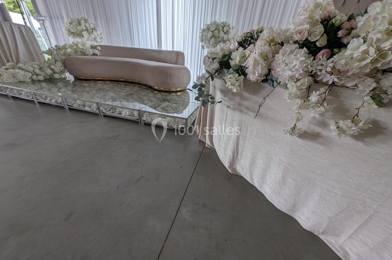 Canapé beige et table basse en verre entourés de bouquets de fleurs blanches et roses dans une salle décorée.