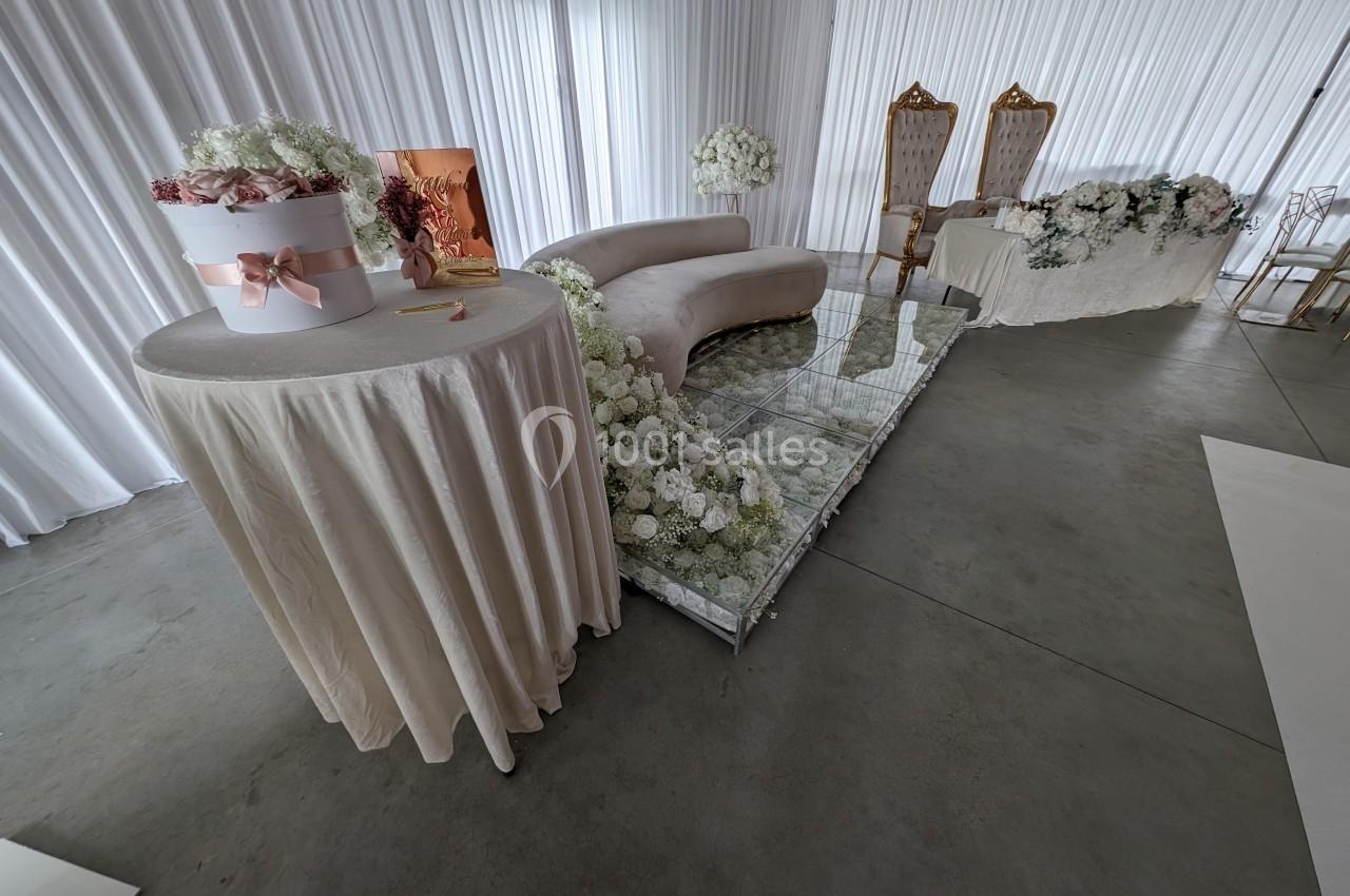 Salle décorée pour un événement avec fauteuils dorés, table ornée de fleurs blanches et table ronde avec bouquet.