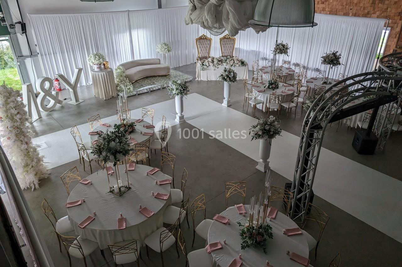 Salle de réception décorée pour un mariage, avec tables rondes, chaises dorées, nappes blanches et arrangements floraux.