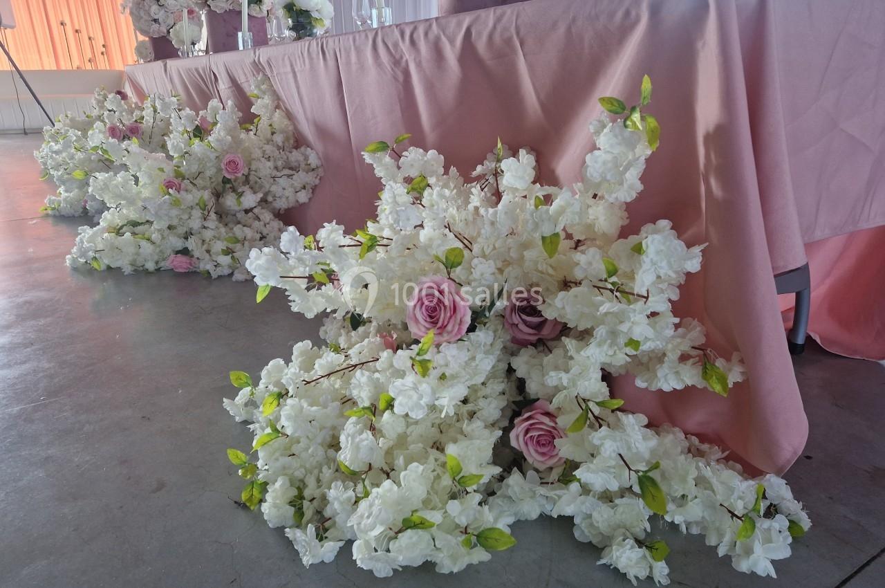 Décoration florale composée de roses roses et de fleurs blanches disposées au sol devant une table drapée de tissu rose.