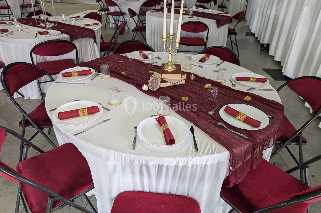 Table ronde décorée avec une nappe blanche, un chemin de table bordeaux, des serviettes rouges et un chandelier doré.