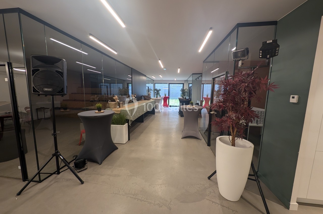 Salle moderne avec tables dressées, plantes décoratives et équipements audio, éclairée par des lumières au plafond.