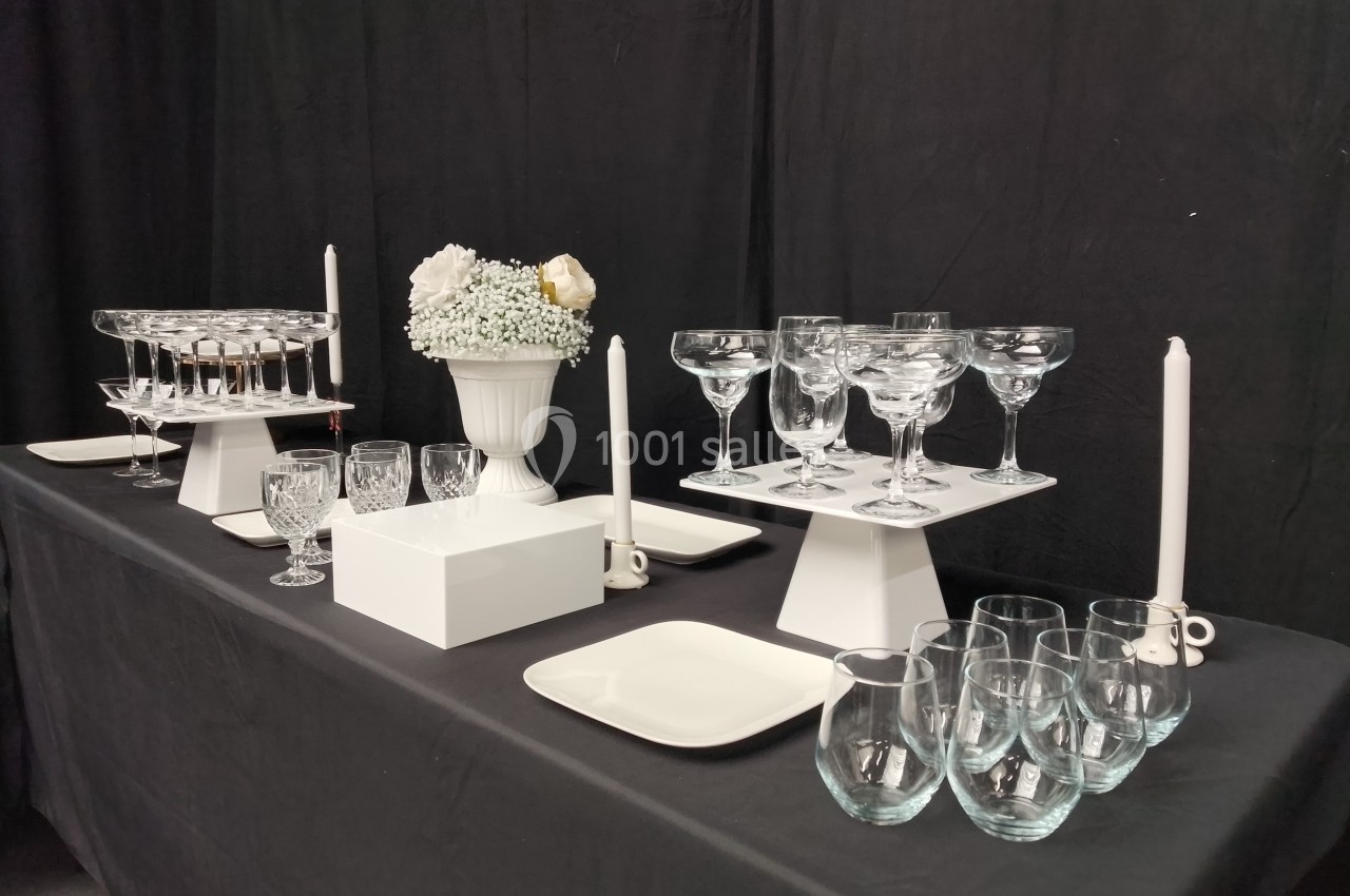 Table dressée avec nappes noires, verres transparents, bougies blanches et un vase de fleurs blanches.
