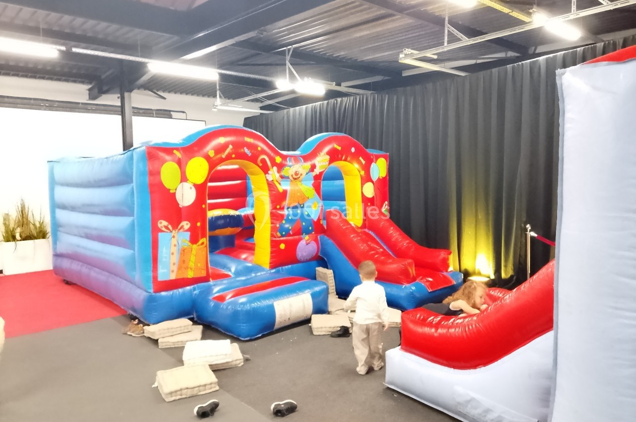 Structure gonflable colorée avec toboggans, décorée de motifs festifs, utilisée par deux jeunes enfants dans une salle…