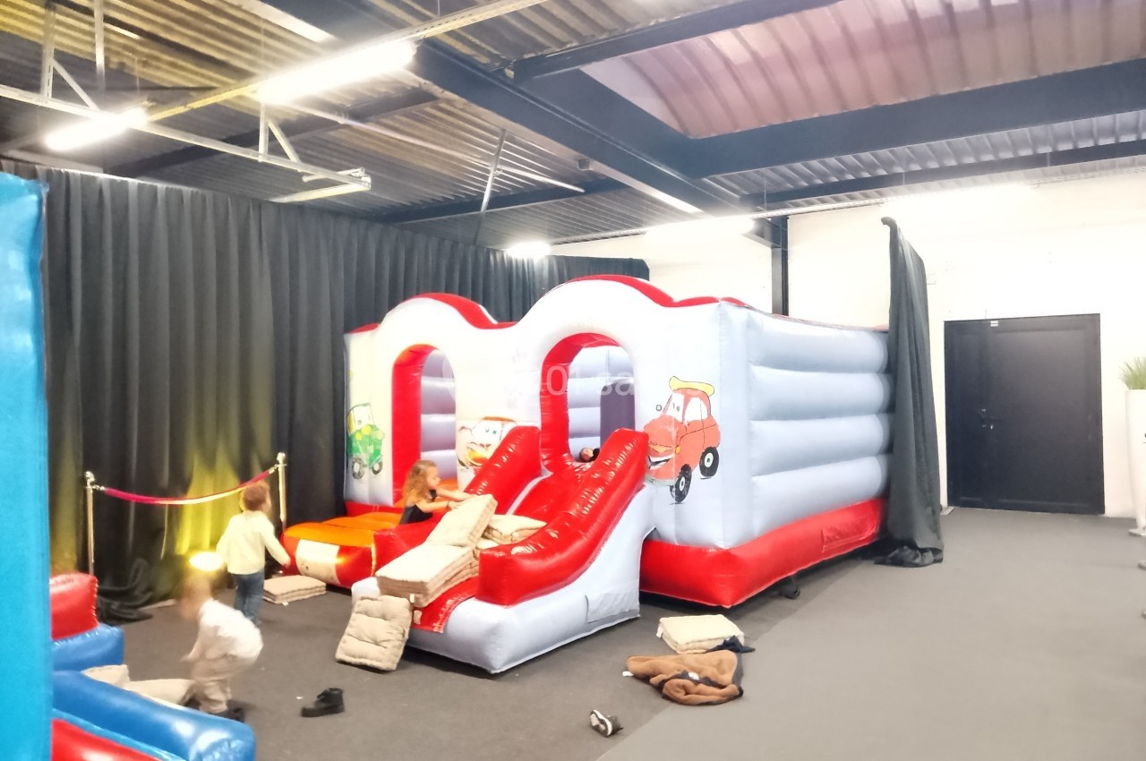 Structure gonflable colorée avec toboggans, entourée d'enfants jouant dans une salle intérieure éclairée.