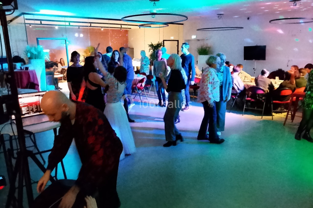 Personnes dansant et discutant dans une salle éclairée par des lumières colorées lors d'un événement festif.