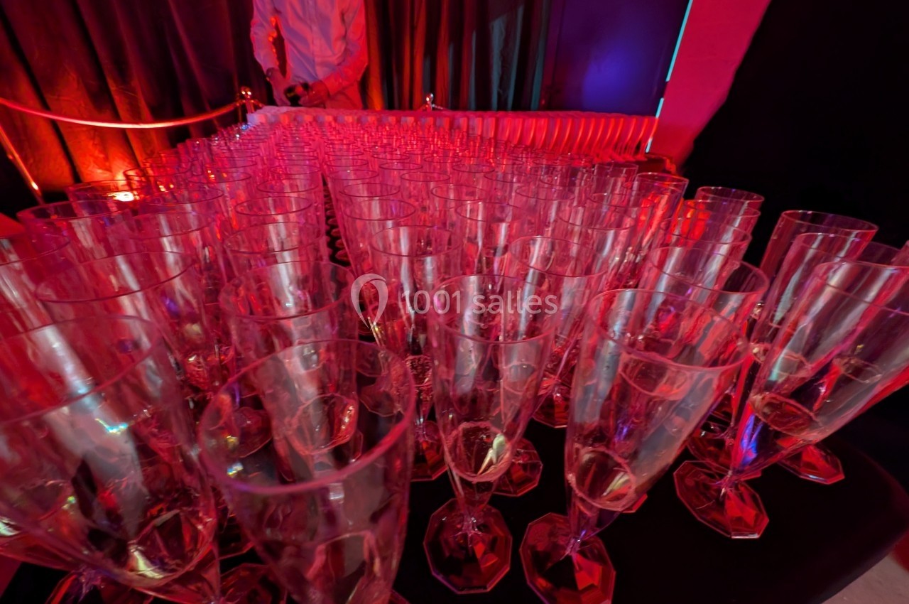 Rangée de flûtes à champagne vides alignées sur une table dans une ambiance lumineuse rouge.