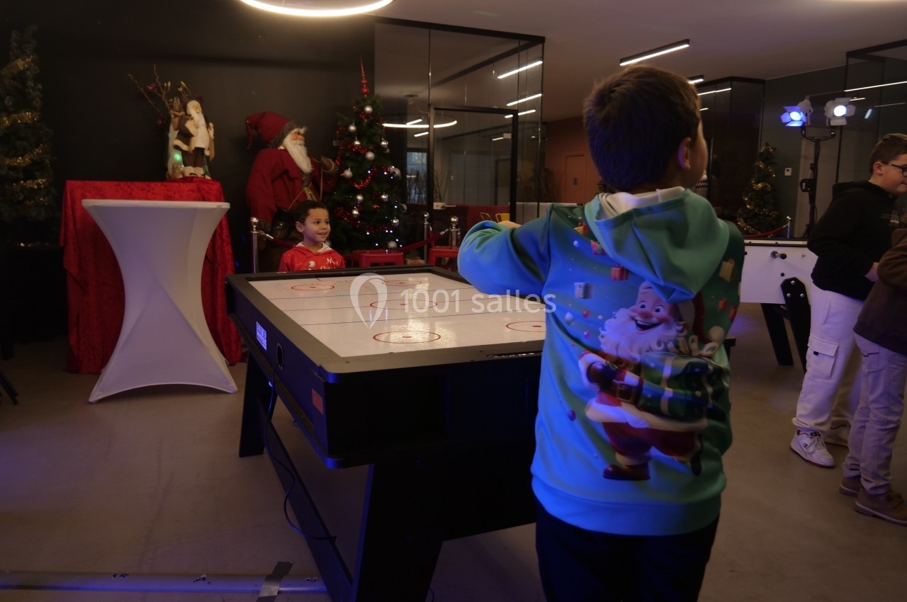 Deux enfants jouent à un jeu de hockey sur table dans une salle décorée pour Noël avec un sapin et un Père Noël.